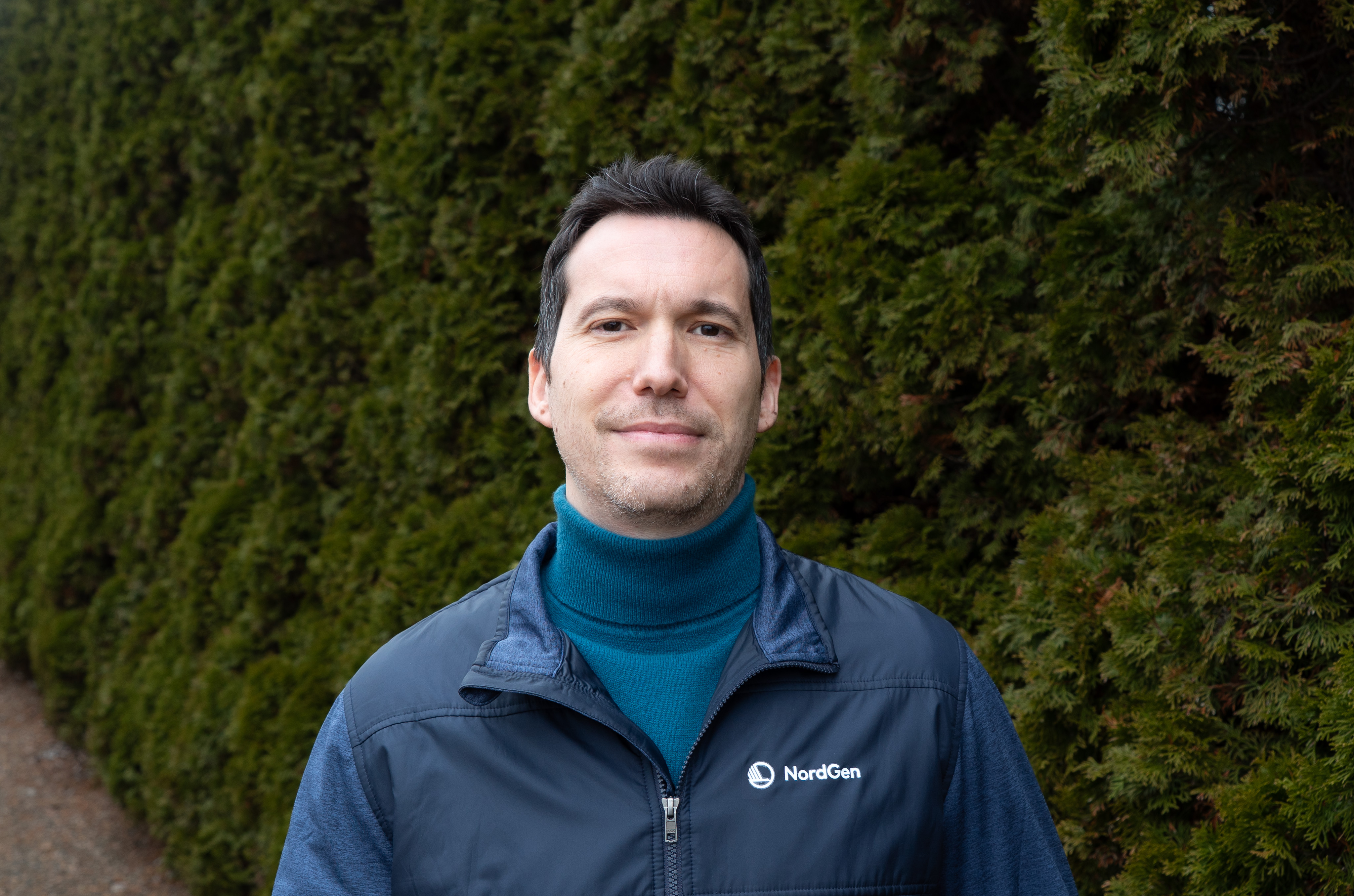 Man ståendes framför en grön häck.