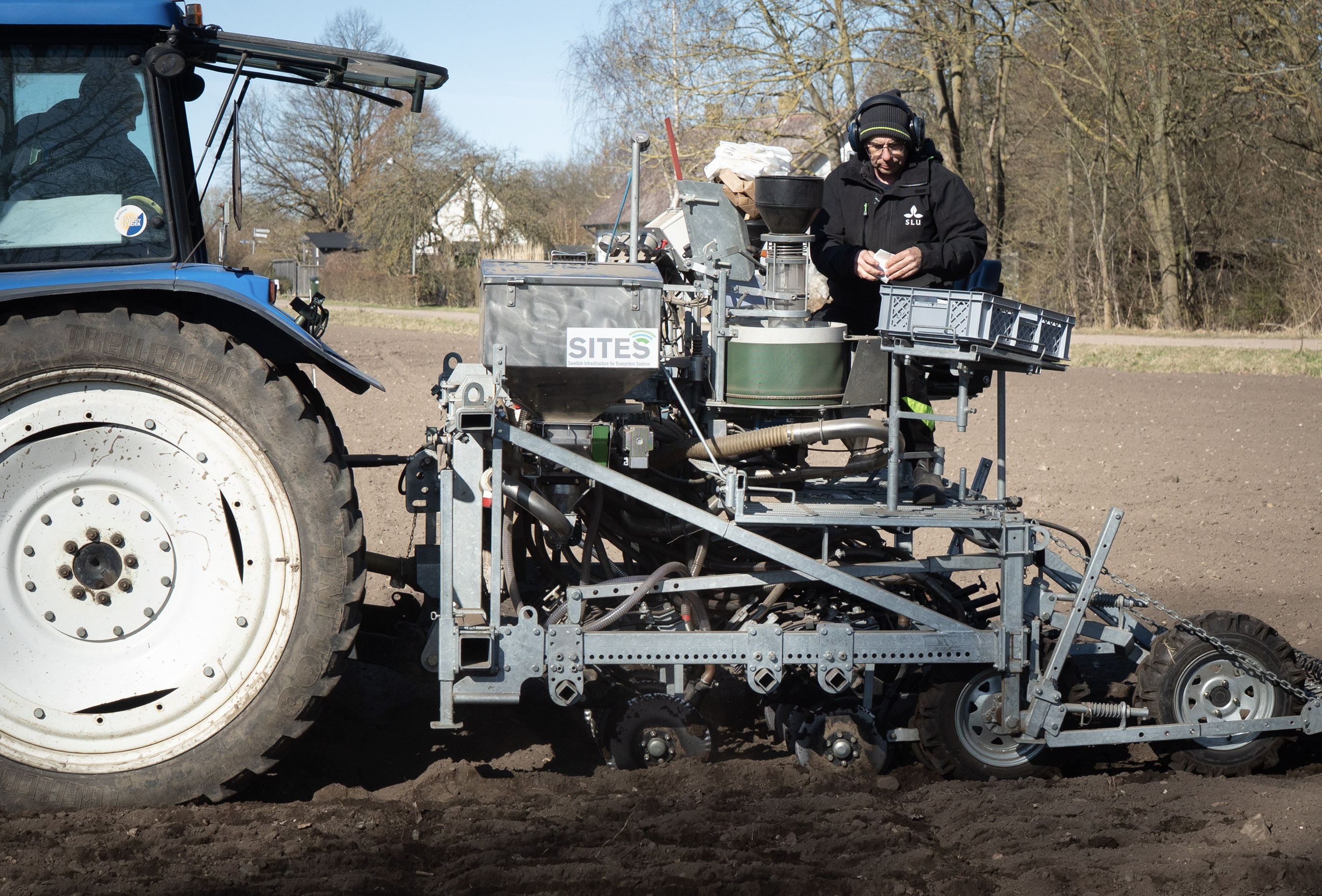 Man sowing seeds behind tractor.