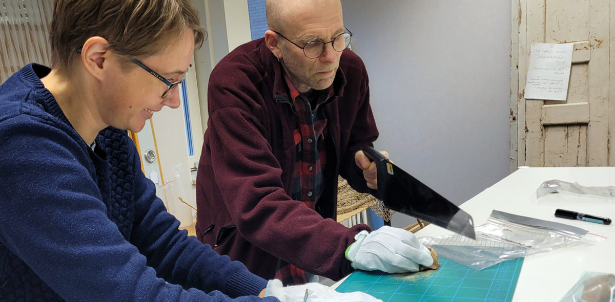 Två arkeologer vid ett arbetsbord sågar i gamla djurben för att få fram DNA-material
