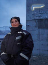 Woman in svart overall standing in front of the Seed Vault exterior 